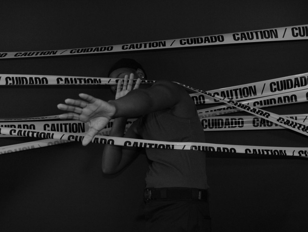 Dramatic black and white image of person behind caution tape, conveying restriction and alertness.