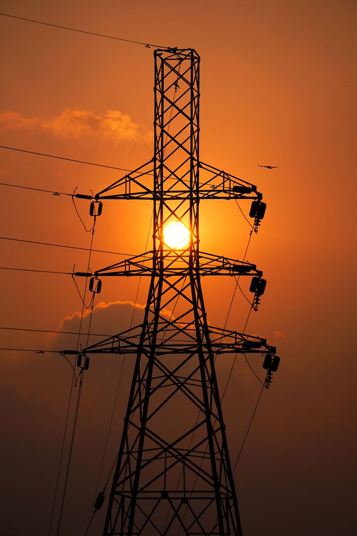 A striking silhouette of a transmission tower against a vibrant sunset sky.