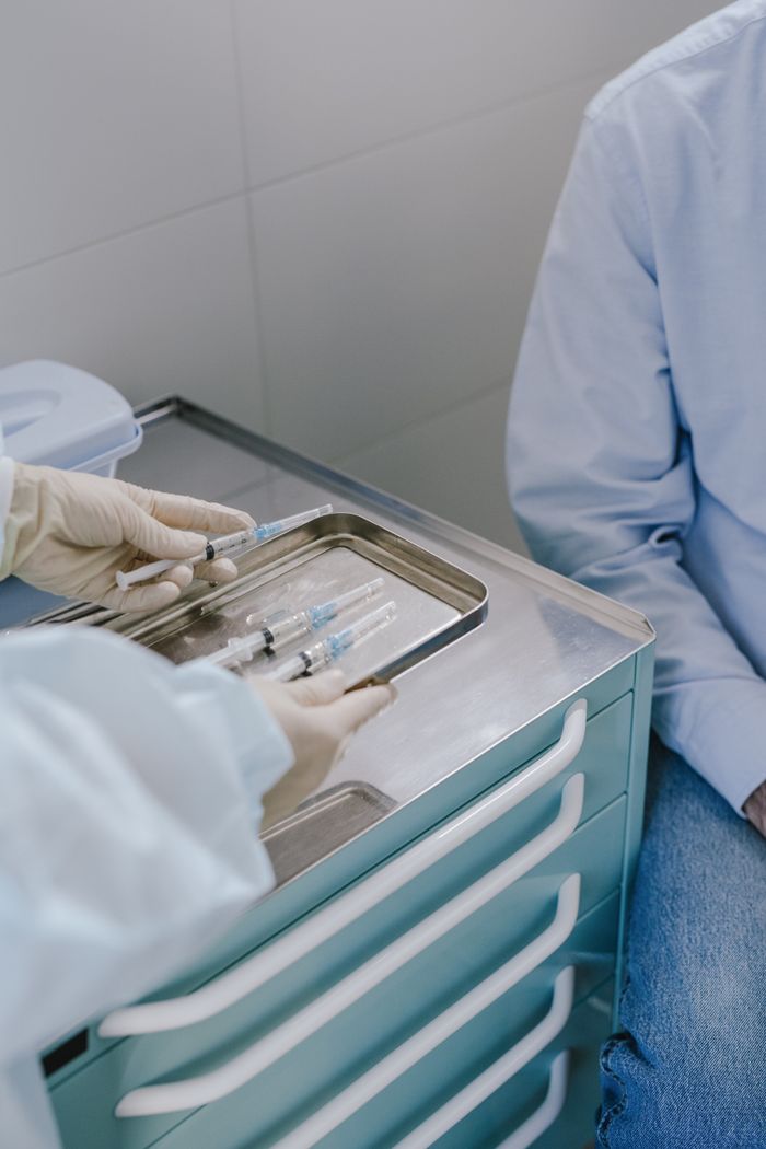 Doctor prepares syringes on a tray for a patient in a clinical setting.