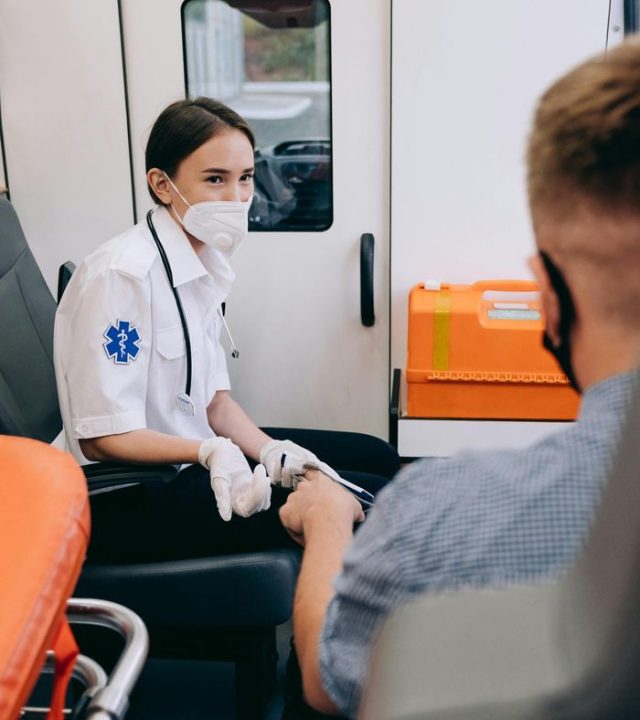 A paramedic wearing a mask assists a patient inside an ambulance, ensuring safety and care.